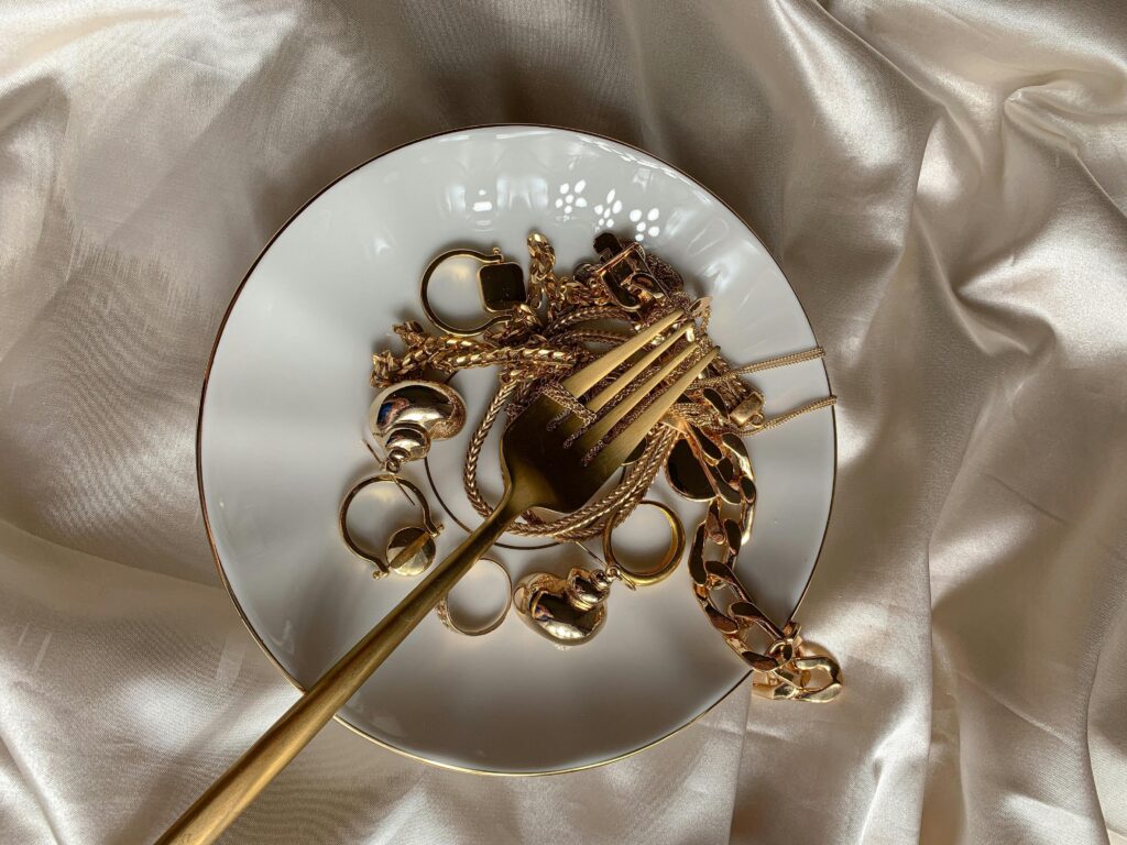 A close-up of luxurious gold jewelry on a ceramic plate with satin fabric backdrop.